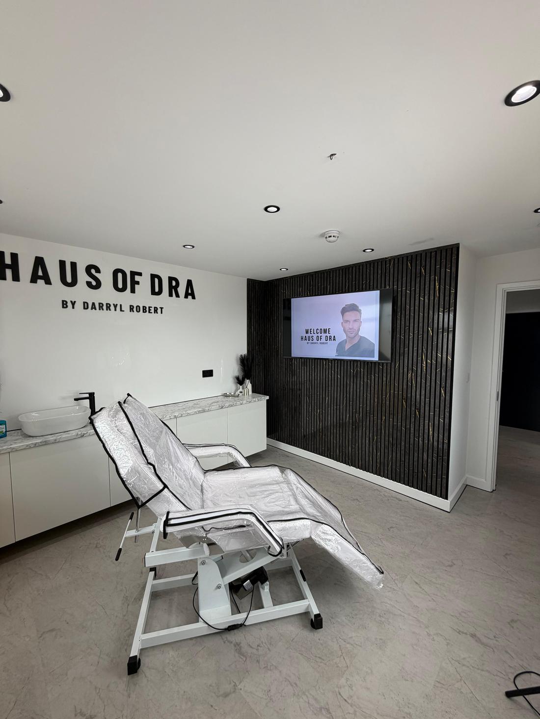 A treatment room at HAUS of DRA with the brand lettering on a white wall and dark fluted panelling.