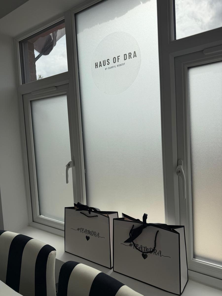 Frosted window glass carrying the HAUS of DRA emblem, with branded client bags on the sill.